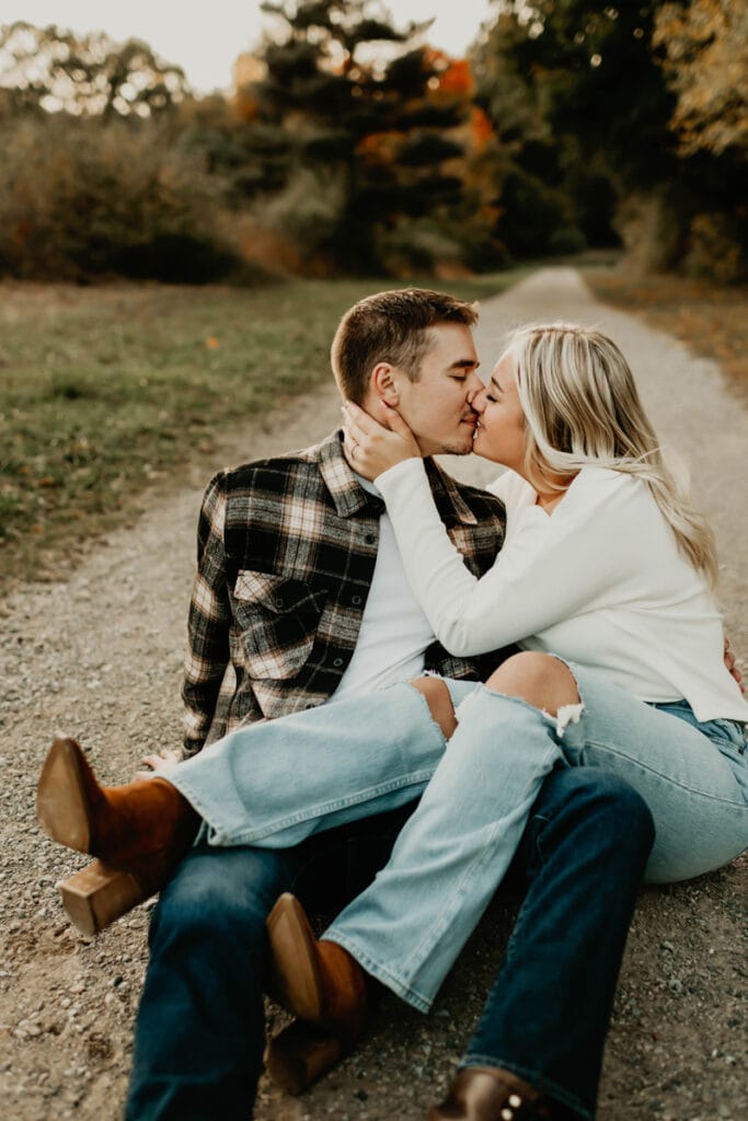 Family Photographer, a young couple sit on a rock beside a country path and kiss.