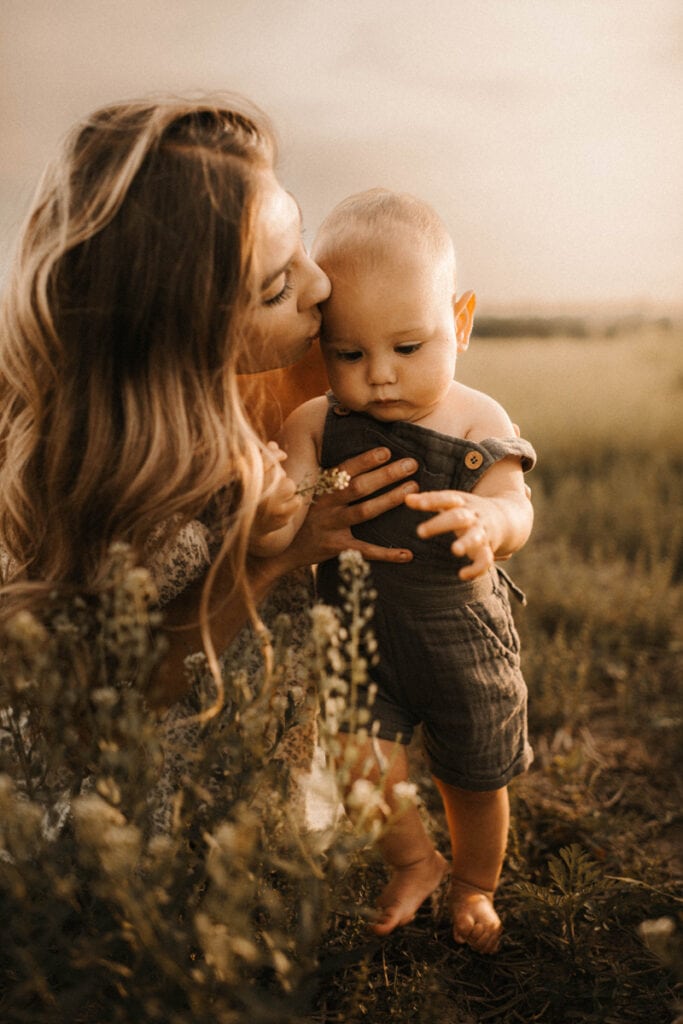 Family Photographer, a mother kisses her baby in a grassy field
